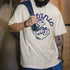 Person wearing a white t-shirt with blue graphic design and text, holding a blue jacket.